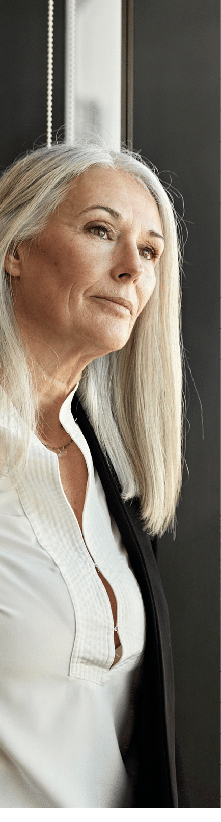 Waist-up view of mature Caucasian woman in businesswear enjoying a private moment for contemplation as she looks at downtown district from high angle.