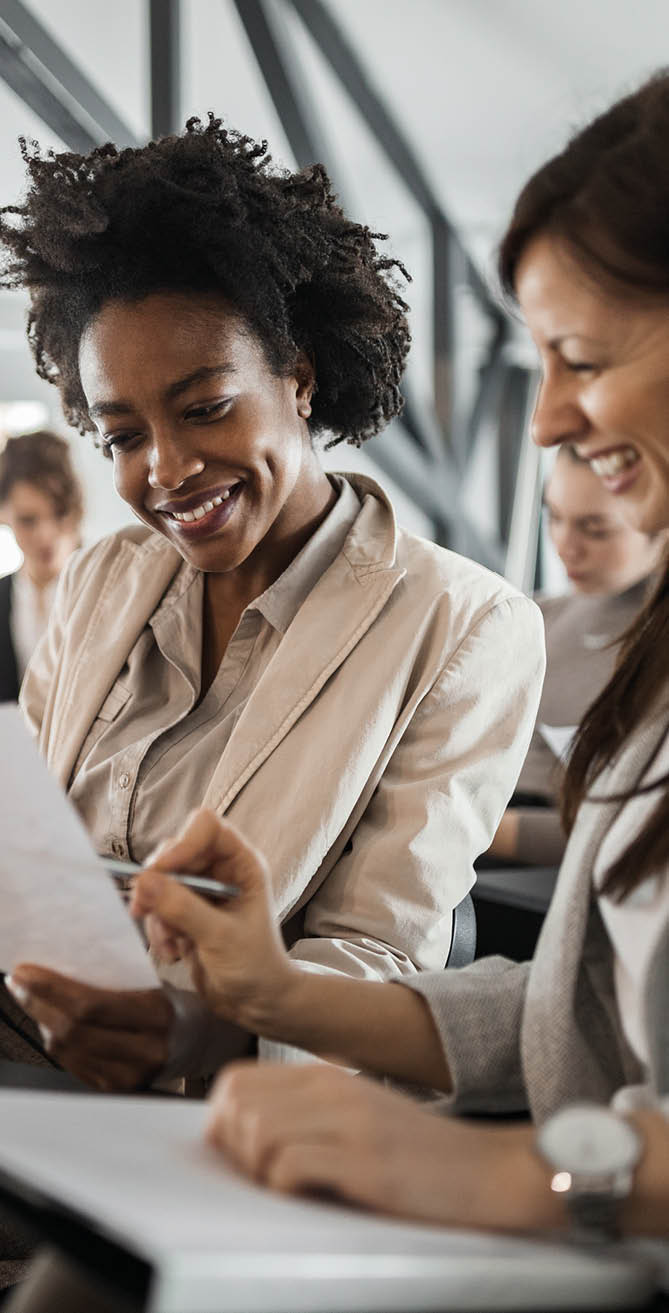 Two females in a suits, doing paper work.